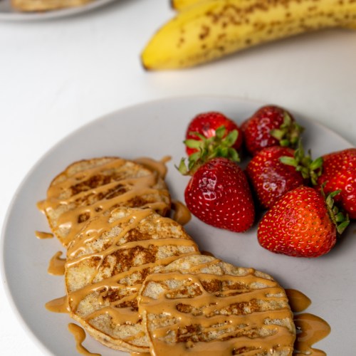 plate of baby banana pancakes with peanut butter on top and strawberries on the side
