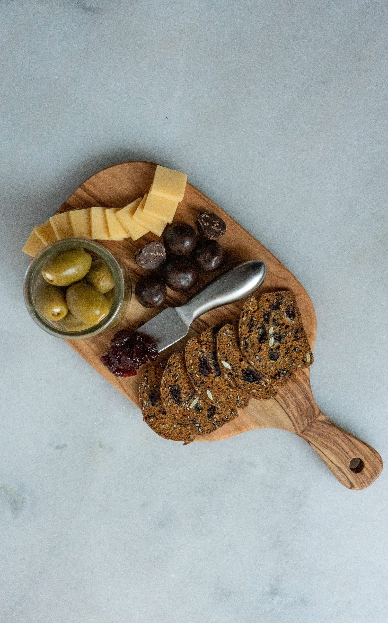Small charcuterie board with olives, cheese, fig crackers, spiced cherry jam and chocolates