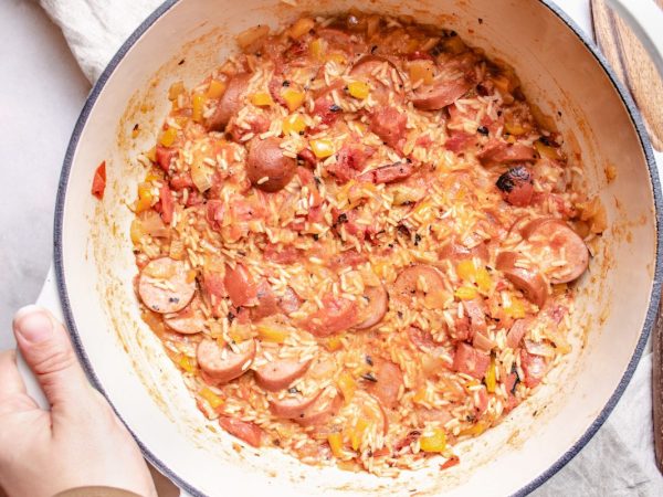 large white dutch oven with jambalaya inside with a womans left hand holding the pot