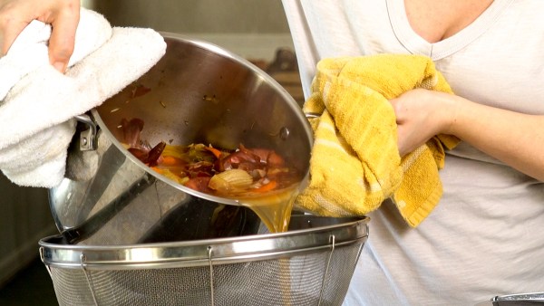girl pouring homemade vegetable broth from scraps through a strainer