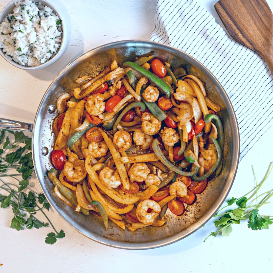 shrimp with rice bowl recipe shrimp and bell peppers and tomatoes in a silver skillet with cilantro on the sides and cilantro lime rice in the corner
