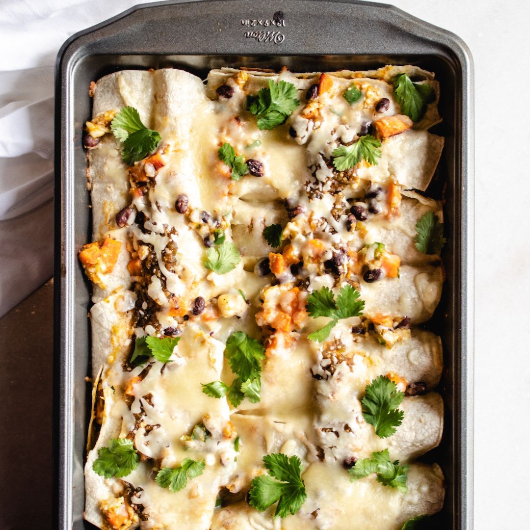 sweet potato black bean enchiladas with cilantro greens on top in a dark pan over a white cloth
