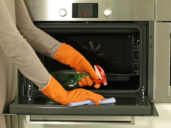 person wearing orange cleaning cloves and scrubbing their oven door