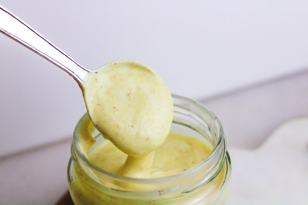silver spoon scooping honey yogurt mustard sauce out of a glass jar on white background