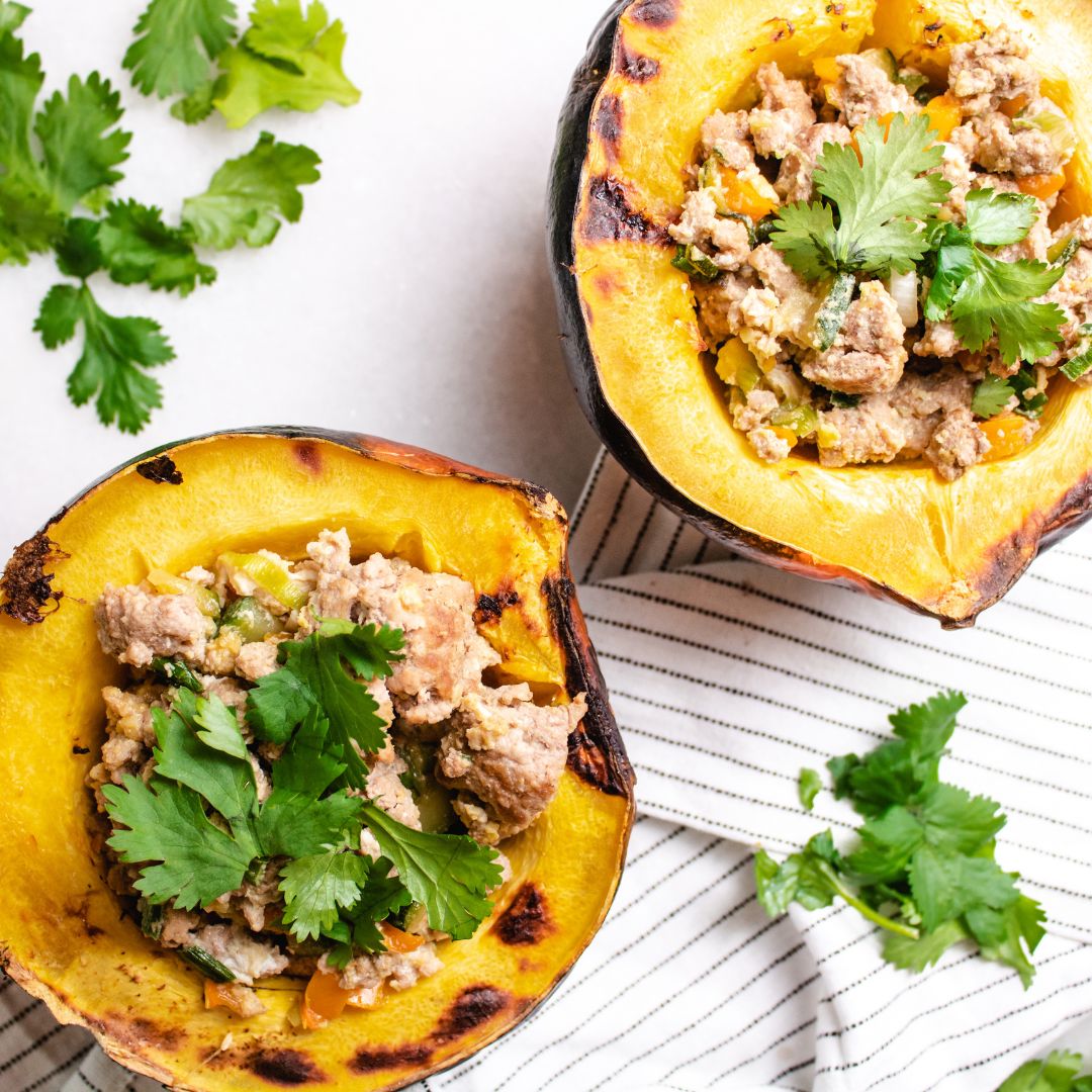 acorn squash stuffed with chorizo and vegetables with cilantro on top and on the sides with white background