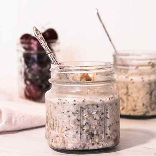 two mason jars with overnight cherry oats inside them and cherries in the background
