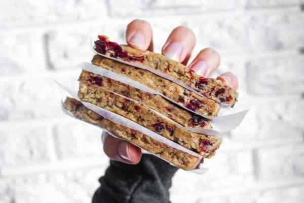 woman's hand holding five stacked homemade sunflower butter granola bars with craisins